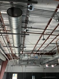 Exposed HVAC ductwork, electrical conduits, and structural beams on the ceiling of an unfinished industrial building interior.