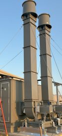 Tall vertical exhaust stacks on a rooftop HVAC system, secured with support cables against a clear sky.