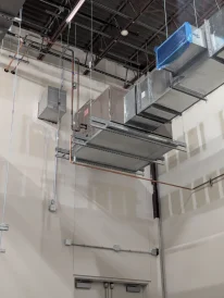 Suspended metal air ducts and copper piping installed near the ceiling of a commercial building.