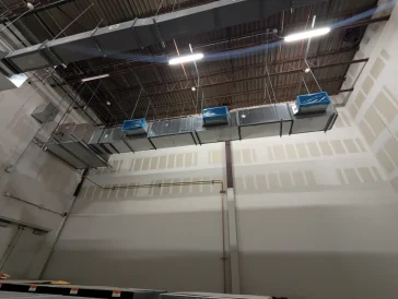 Wide view of industrial HVAC ductwork and lighting suspended from a warehouse ceiling.
